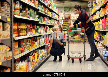 Ein junges Paar in einem großen Supermarkt, mit einem Wagen, zu Fuß durch die Gänge mit Regale voller Lebensmittel einkaufen. Stockfoto