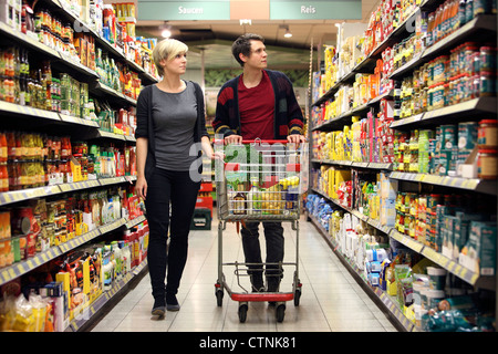 Ein junges Paar in einem großen Supermarkt, mit einem Wagen, zu Fuß durch die Gänge mit Regale voller Lebensmittel einkaufen. Stockfoto