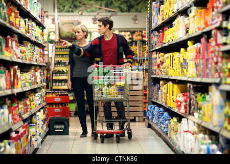 Ein junges Paar in einem großen Supermarkt, mit einem Wagen, zu Fuß durch die Gänge mit Regale voller Lebensmittel einkaufen. Stockfoto