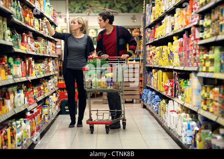 Ein junges Paar in einem großen Supermarkt, mit einem Wagen, zu Fuß durch die Gänge mit Regale voller Lebensmittel einkaufen. Stockfoto