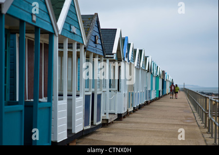 Blaue und grüne Strandhütten in Southwold, Suffolk, UK mit paar in Ferne unscharf Stockfoto