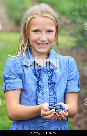 Junges Blonde Mädchen hält frisch gepflückt Blaubeeren in einem blauen Kleid lächelnd Stockfoto