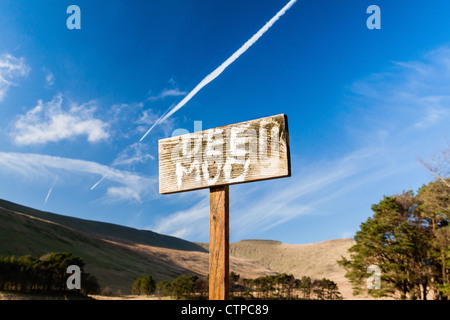 Ein handgemaltes Schild an einem Holzstab Warnung Menschen in tiefen Schlamm an einem See in einem Nationalpark in Wales.  Ein Jet Trail oben. Stockfoto