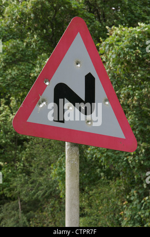 Eine britische Verkehrszeichen Warnung vor einer doppelten Biegung voraus. In ländlichen Dorset wurde beschossen und gespickt mit Einschusslöchern. England, United Kingdom. Stockfoto