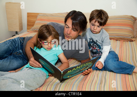 Vater, Tochter und Sohn liegen auf dem Bett ein Buch zu lesen. Stockfoto
