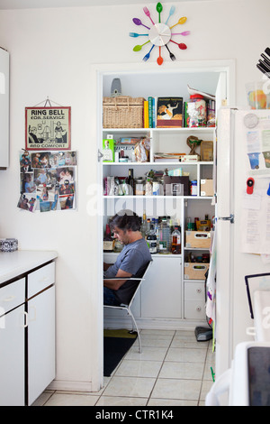 Ein Mann sitzt an einem kleinen Schreibtisch in einer Küche Pantry. Stockfoto