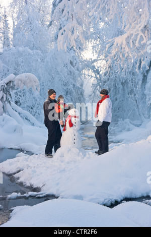 Mann, der seine Tochter hält Hut aufgesetzt Schneemann während seiner Frau Frost bedeckt Bäume im Hintergrund Russisch Jack Springs Uhren Stockfoto