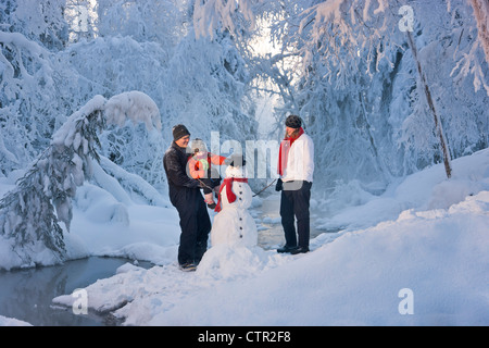 Mann, der seine Tochter hält Hut aufgesetzt Schneemann während seiner Frau Frost bedeckt Bäume im Hintergrund Russisch Jack Springs Uhren Stockfoto