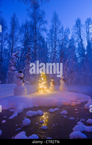 Schneemann Familie stehen nächsten Weihnachtsbaum auf Schnee bedeckte Insel in mittleren kleinen Bach in Raureif bedeckt Wald Dämmerung Stockfoto