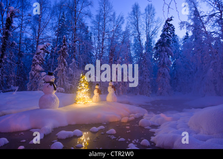 Schneemann Familie stehen nächsten Weihnachtsbaum auf Schnee bedeckte Insel in mittleren kleinen Bach in Raureif bedeckt Wald Dämmerung Stockfoto