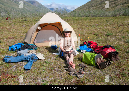 Reife Frauen Camper entspannt durch Zelt an sonnigen Tag am Marsh Fork Canning River in Brooks Range Arctic National Wildlife Refuge Stockfoto