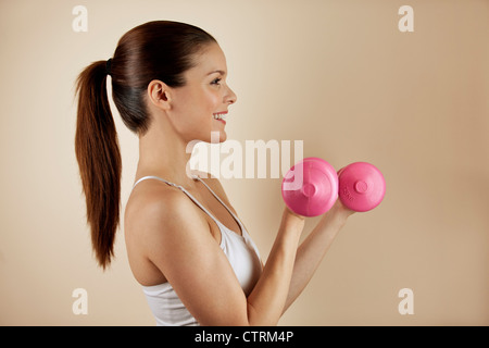 Eine junge Frau, die das Training mit rosa Hanteln, Seitenansicht Stockfoto