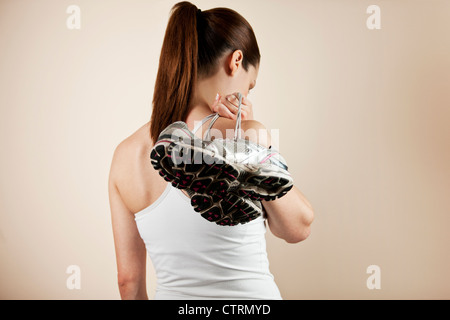 Eine junge Frau trägt ein paar Trainingsschuhe über ihre Schulter, blickte Stockfoto