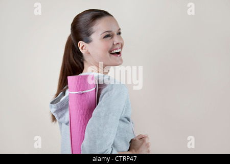 Eine junge Frau trägt eine Yoga-Matte, lachen Stockfoto