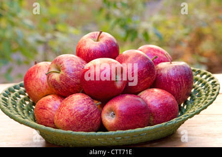 Rote Äpfel in einem grünen Korb auf Holztisch Stockfoto