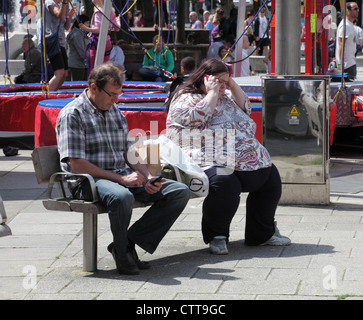 Mann und beleibte Frau auf der Bank sitzen und mit Handys Portsmouth, England, UK Stockfoto