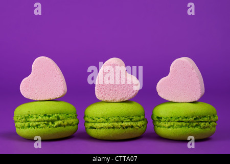 Pistazien-Makronen und herzförmigen Bonbons auf lila Hintergrund Stockfoto