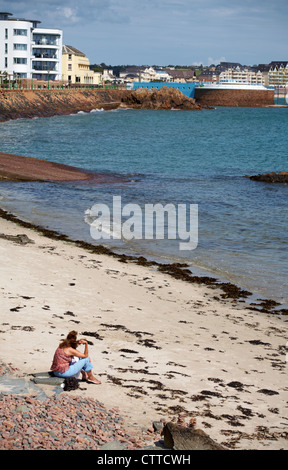 Junge Frau sitzt auf Felsen am Strand von St. Helier, Jersey im Juli Stockfoto