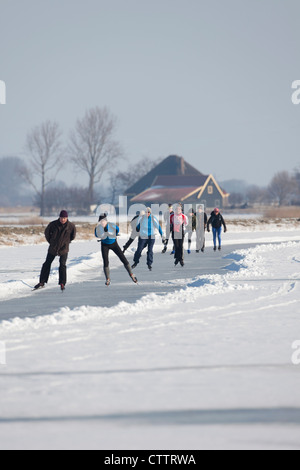 Niederlande, Jisp, Winter. Menschen Sie Eislaufen auf dem Polder Kanal vor Bauernhof. Stockfoto