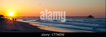 Paare, die die Hunde am Strand mit einem genialen Sonnenaufgang/Sonnenuntergang vor ihnen. Stockfoto