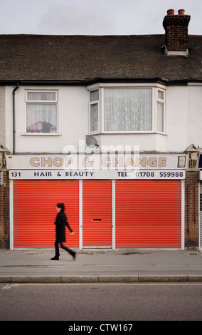 Eine Frau, die einen geschlossenen Schönheitssalon mit roten Fensterläden in Rainham Essex vorbeigehen. Stockfoto