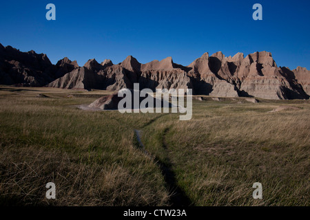 Wanderweg durch Wiesen zu Felsformationen, Badlands Nationalpark, South Dakota, Vereinigte Staaten von Amerika Stockfoto
