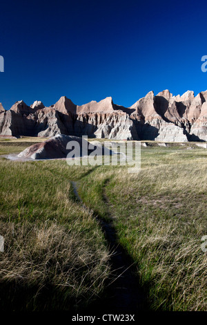 Wanderweg durch Wiesen zu Felsformationen, Badlands Nationalpark, South Dakota, Vereinigte Staaten von Amerika Stockfoto