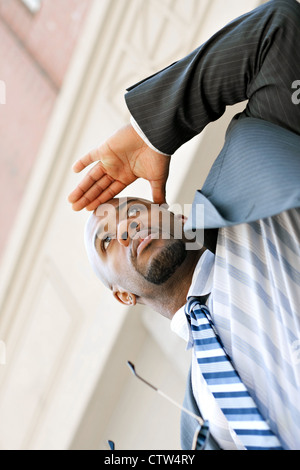 Ein junger Geschäftsmann hält seine Hand an die Stirn, als er sich etwas in der Ferne ansieht. Stockfoto