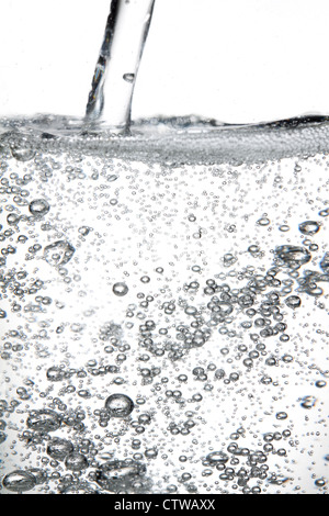 Transparente kohlensäurehaltige Getränke in einem durchsichtigen Behälter, geschossen auf weißem Hintergrund gegossen. Stockfoto