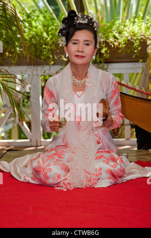 Myanmar, Burma. Bagan. Burmesische Tänzerin in traditioneller Kleidung, sitzen, halten ein kleines Schlaginstrument und zwei kleine Glocken. Stockfoto