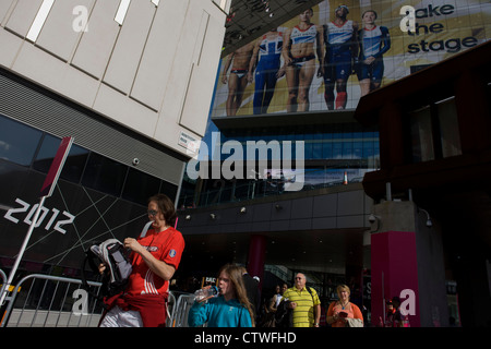 Ein Zuschauer kommt mit einem Ticket im Mund im Einkaufszentrum Westfield Stratford nahe dem Eingang des Olympiaparks während der Olympischen Spiele 2012 in London. Über ihren Köpfen sind Team GB Sportler - riesige Figuren von Jessica Ennis, Tom Daley und andere. Westfield befindet sich am Rande des Olympiaparks, Europas größtes städtisches Einkaufszentrum. Die £1 .45bn Komplex beherbergt mehr als 300 Geschäfte, 70 Restaurants, ein Kino mit 14 Sälen, drei Hotels, eine Kegelbahn und Großbritanniens größte Casino. Stockfoto