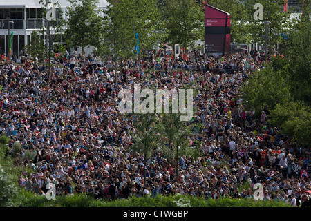 Massen der Zuschauer versammeln sich auf dem Rasen im Olympiapark, großen TV-Bildschirmen von live-Sport-Berichterstattung während der Olympischen Spiele 2012 in London zu sehen. Die Anpflanzung von 4.000 Bäume, 300.000 Feuchtgebietspflanzen und mehr als 150.000 Stauden sowie nektarreichen Wildblumen sorgen für eine farbenfrohe Kulisse für die Spiele. Dieses Land wurde umgestaltet, um eine 2,5 qkm sportliche Komplex, einmal Industriebetriebe und nun Austragungsort der acht Orte, darunter die Hauptarena Aquatics Centre und Velodrom sowie der Athleten Olympisches Dorf werden. Nach den Olympischen Spielen ist der Park als Queen Elizabeth Olympic Park bekannt. Stockfoto