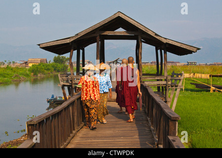 BIRMANISCHE WOWMEN und buddhistische Mönche verwenden die angehobenen Gehweg in der Nähe von MAING THAUK auf dem Weg zum Wochenmarkt - INLE-See, MYANMAR Stockfoto