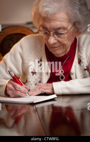 Ältere Frau an einem Tisch sitzen und einen Brief zu schreiben Stockfoto