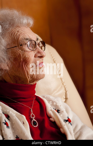 Ältere Frau zu Hause auf Stuhl sitzend und wegsehen Stockfoto