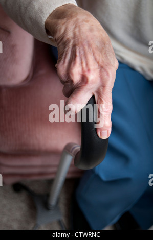 Ältere Frau ist faltig Händen umklammert einen Gehstock zu Hause Stockfoto