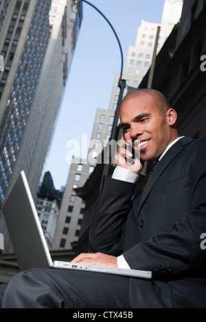 Lächelnde Geschäftsmann mit Laptop während des Gesprächs auf Handy Stockfoto