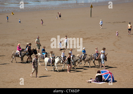 Eselreiten am Strand vorbei an eine Dame mit einem Anschluß-Markierungsfahne Schirm Weston Super Mare Somerset Vereinigtes Königreich Stockfoto