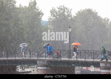Amsterdam-Brücke. Plötzlichen reißenden Sommerregen. Menschen auf einer Brücke mit Sonnenschirmen. Eine lokale in Regenkleidung mit Einkaufstasche. Stockfoto
