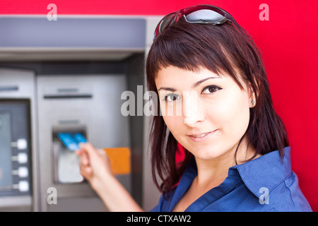 Schöne Frau mit Kreditkarte, sie ist zieht Geld von einem Geldautomaten. Stockfoto