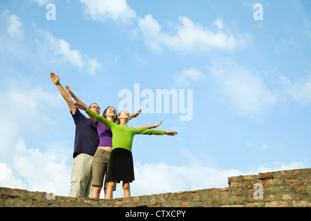 Drei junge Menschen bleiben mit erhobenen Händen gegen blauen Himmel Stockfoto