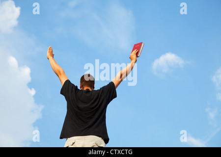 Junger Mann mit erhobenen Händen gegen blauen Himmel Stockfoto