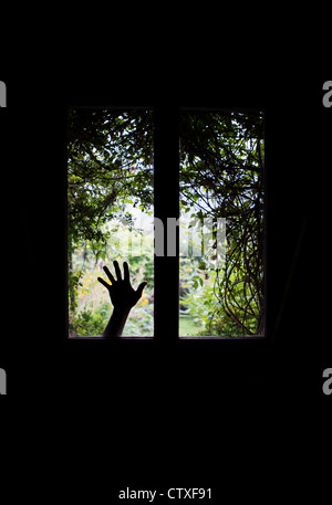 Silhouette Hand gegen Glasfenster in einer Haustür vor einem verwilderten Garten Blick. UK Stockfoto