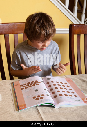 7 Jahre Alter mexikanisch-amerikanischen Grundschule Alter Junge hat Mathe-Hausaufgaben mit Fingern zählen zu Hause Stockfoto