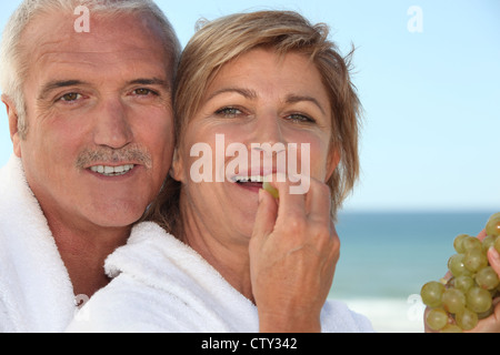 Reife Frau im Bademantel Spa Resort essen Trauben mit Ehemann Stockfoto