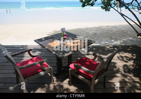 Zwei hölzerne Stühle und Tisch, legte für Mahlzeit auf decking, neben breiten goldenen Sandstrand, zwei Personen am Meer Rand, Koh Sumet. Stockfoto