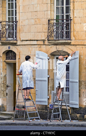 Älteres Ehepaar in Arbeit-Mäntel Malerei Fensterläden - Frankreich. Stockfoto