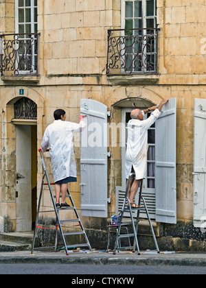 Älteres Ehepaar in Arbeit-Mäntel Malerei Fensterläden - Frankreich. Stockfoto