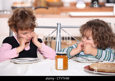 Mürrisch Kinder an einem Tisch mit Pfannkuchen Stockfoto