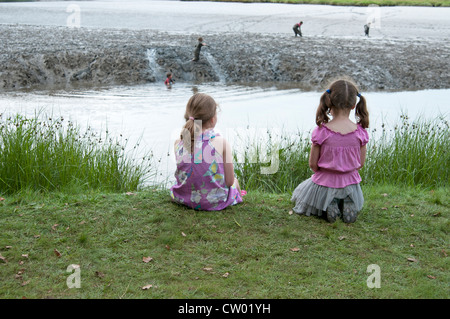 Zwei kleine Mädchen beobachten Kinder spielen in der Mündung Schlamm an den Port Eliot literarische Festival St deutschen Cornwall UK Stockfoto